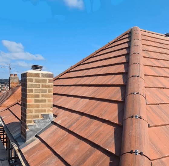 Newly installed red clay tile pitched roof with brick chimney and lead flashing