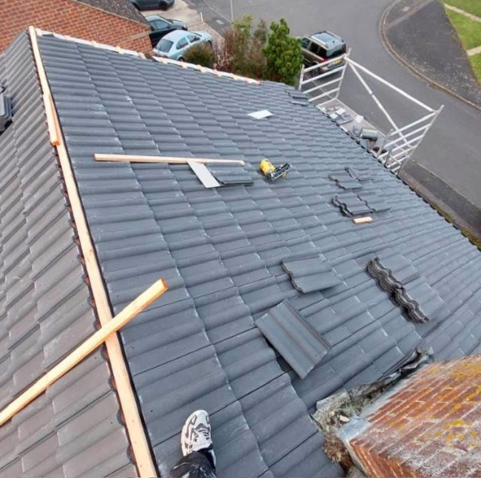 Dark grey tiled pitched roof partially under repair from above