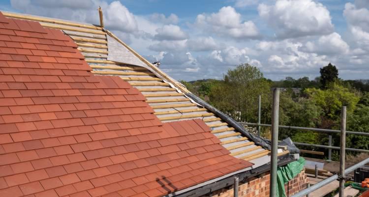 Pitched roof under construction with new red tiles and exposed battens