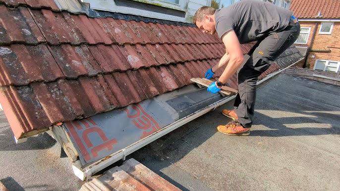 Roofer replacing terracotta tiles on a pitched roof beside a flat-roof section