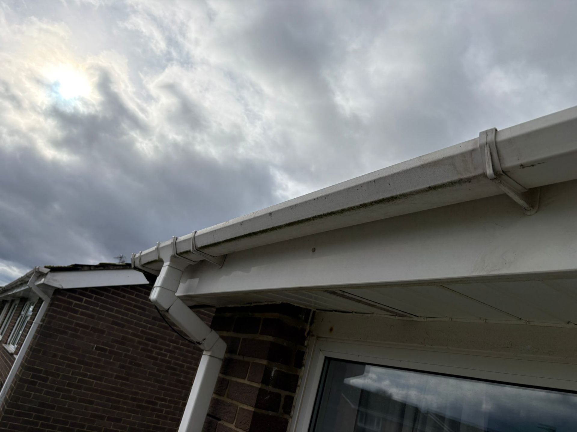 Dirty white uPVC gutters and fascia on a brick house ready for cleaning