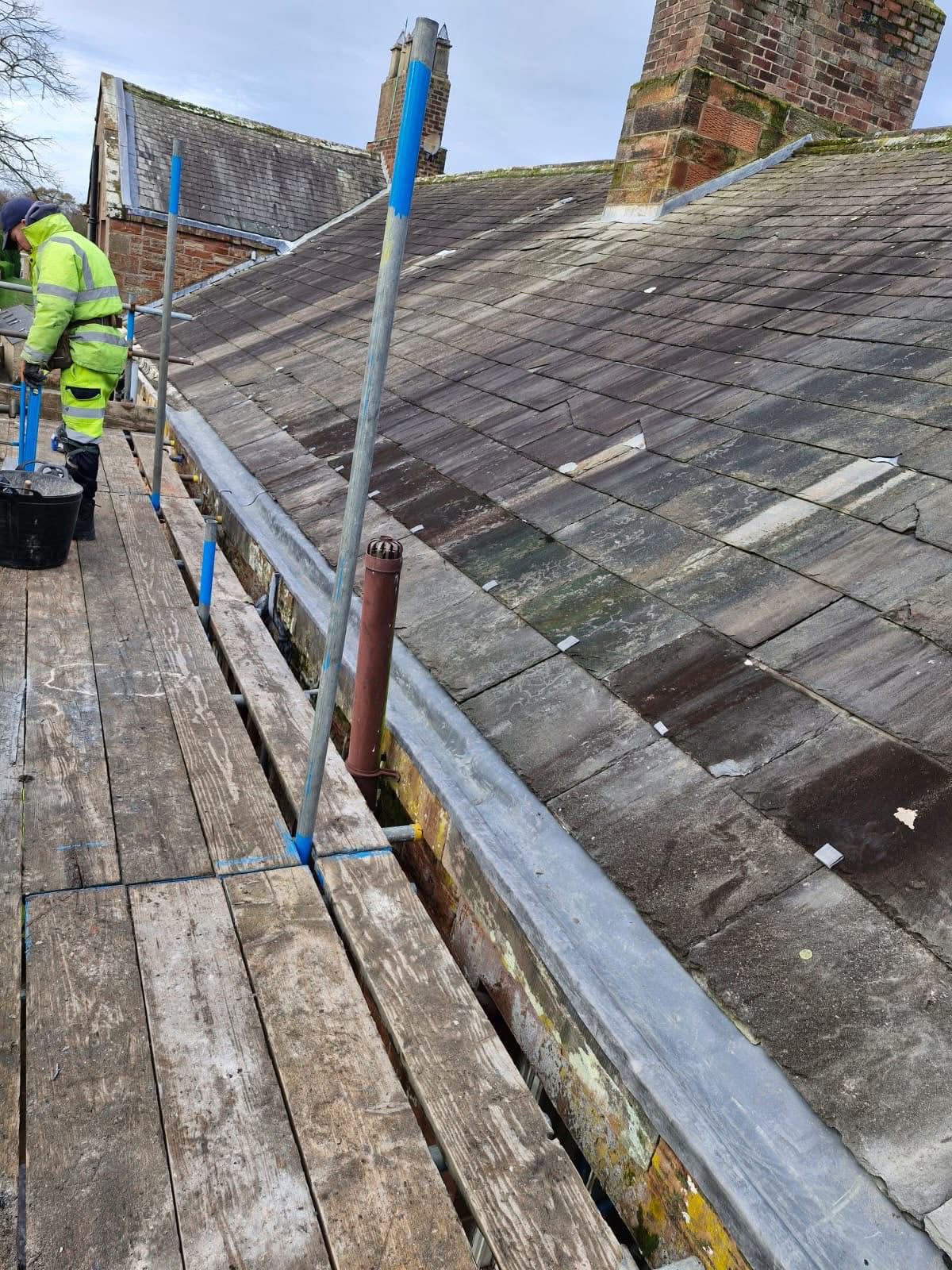 Roofer carrying out pitched roof repair next to a brick chimney