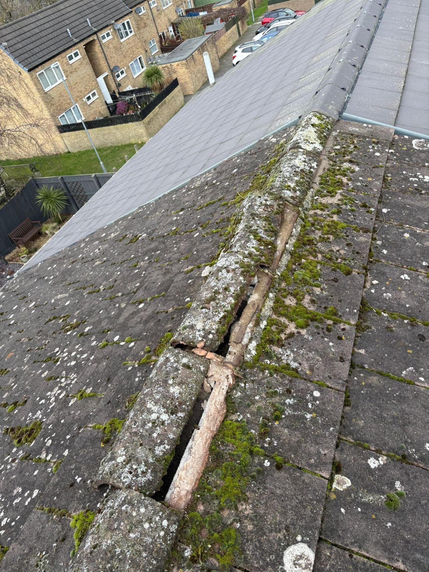 Aerial view of a pitched roof with heavy moss and damaged ridge tiles